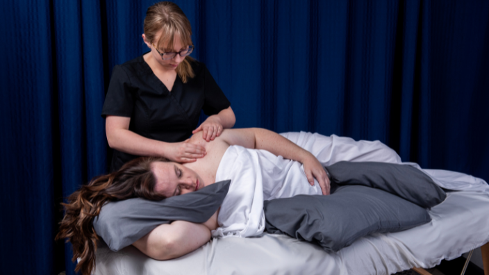 An image of a female massage therapist massaging a pregnant woman who is on a massage table, in the side-lying position.