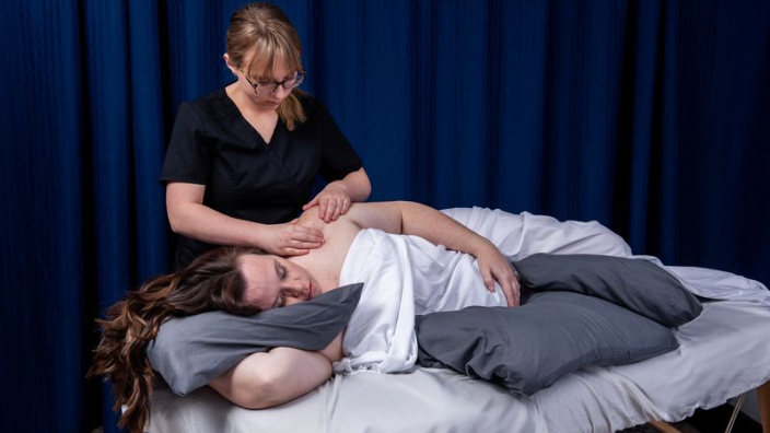 Image of a female massage therapist giving a massage to a woman lying on a table in the side-lying position
