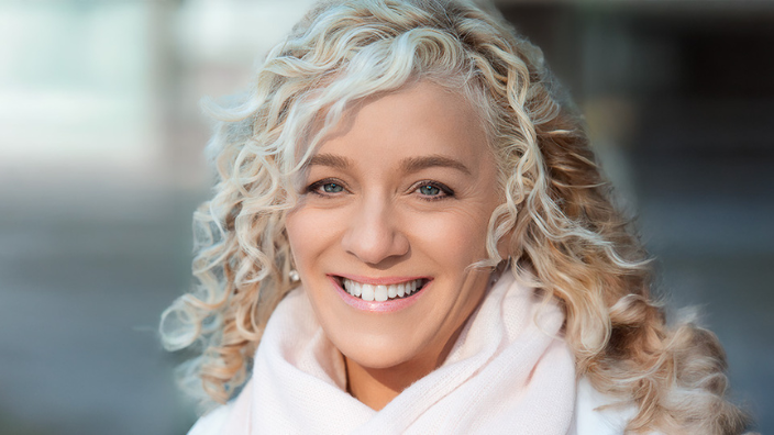 A headshot of Allison Massari, a woman with curly blonde hair; she is smiling and the background is blurred.