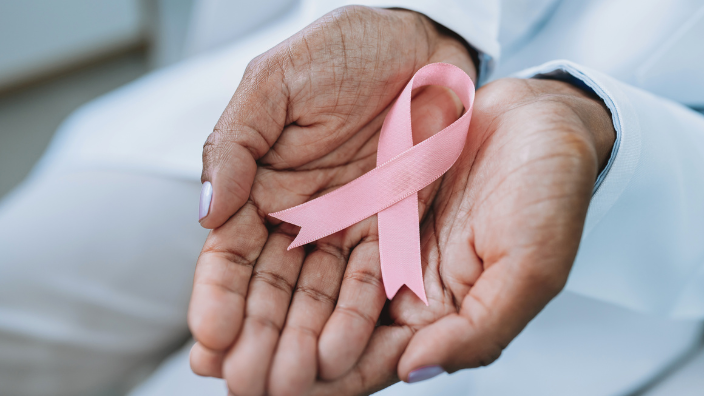 An image of two hands holding a pink ribbon in the Breast Cancer symbol.