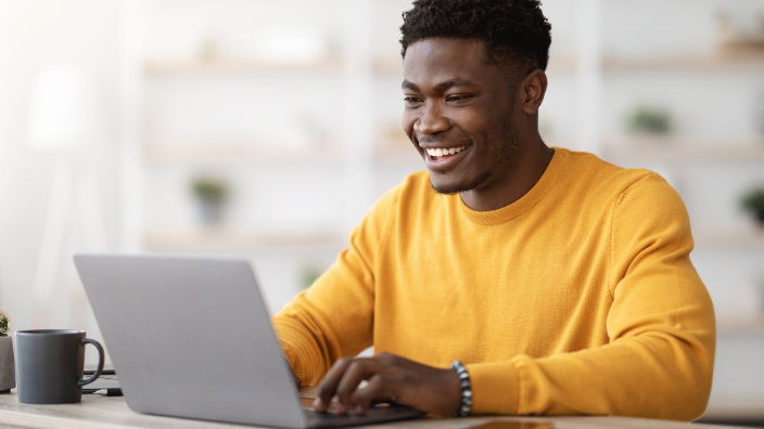 An image of a man smiling and typing on his laptop.