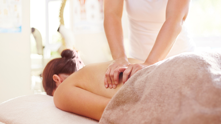 An image of a woman receiving a back massage, she is laying face down with her head in a cradle, the massage therapist is massaging her side.
