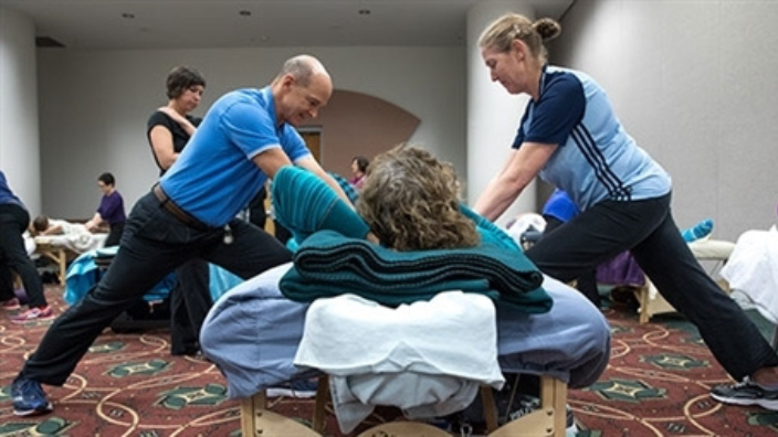 massage workshop in a classroom - image of man and woman practicing massage technique on woman