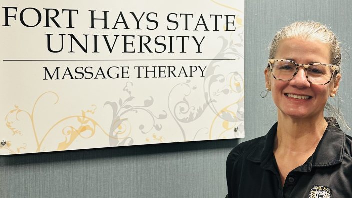older woman posing next to fort hays university sign