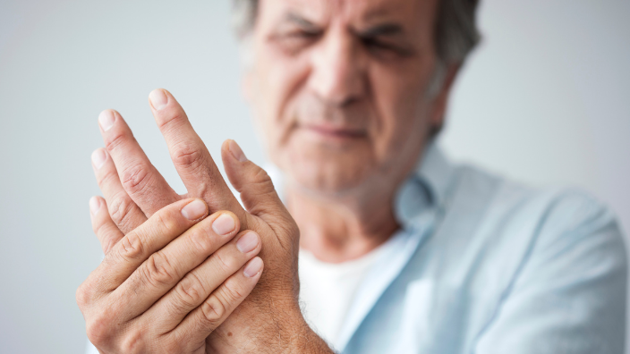 an image of an older man holding his hand in pain.