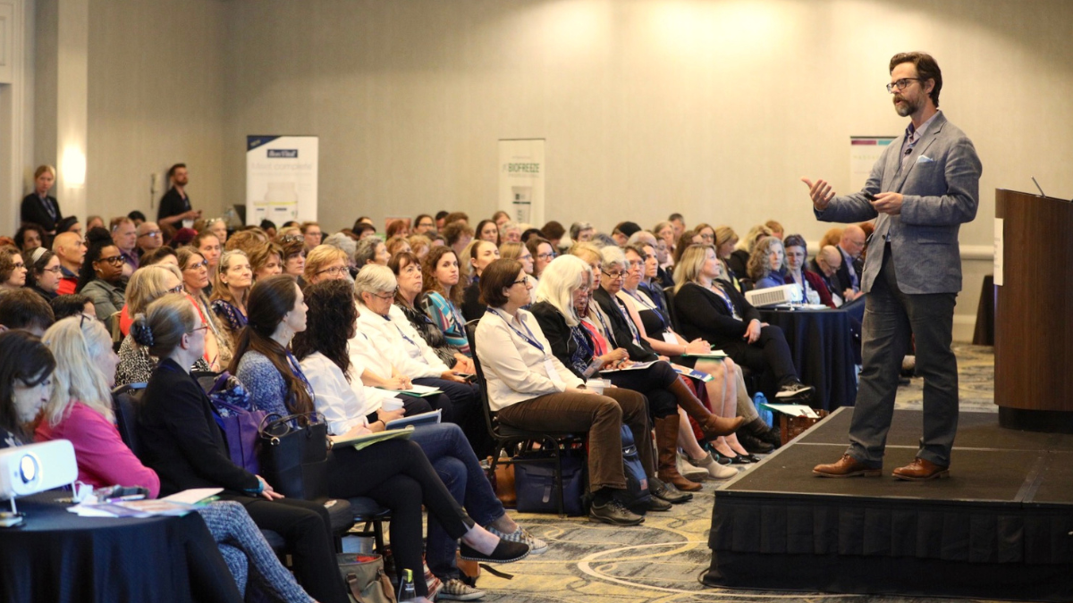 Image of a man standing on a stage speaking to a large audience during IMTRC