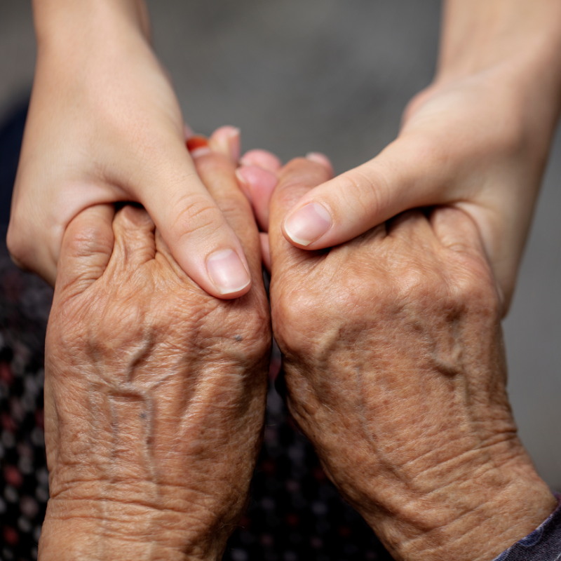 an image of two hands holding the hands of an elderly person.