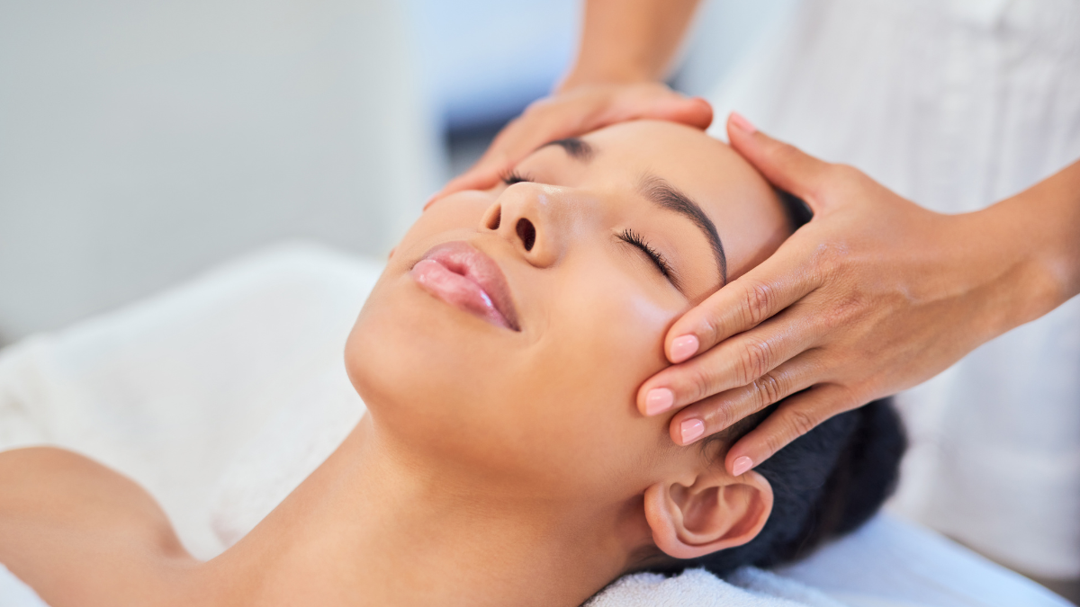 A close-up image of a woman's face as she receives a scalp massage from a massage therapist. She looks calm and relaxed.