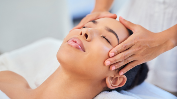 A close up image of a woman's serene face as she receives a scalp massage by a massage therapist.
