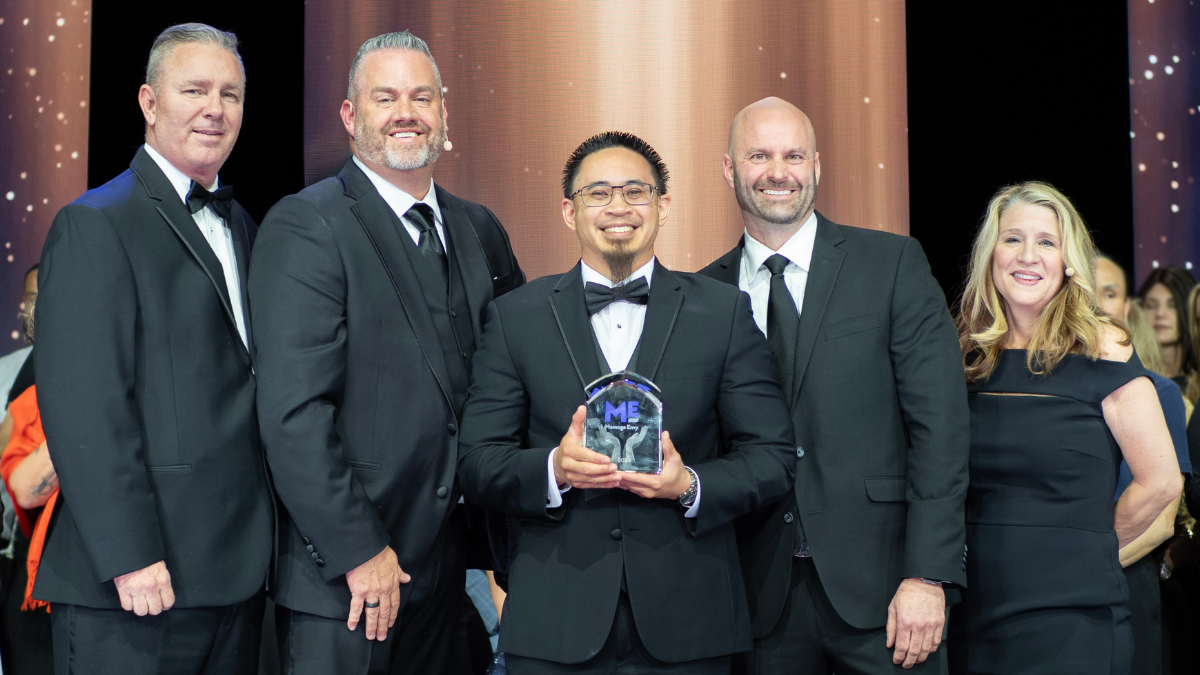 Five people in black-tie attire stand smiling together, the man in the middle holds a trophy.