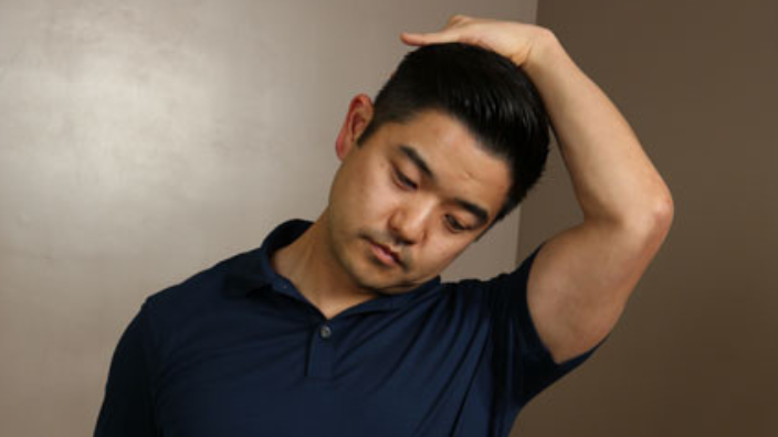 An image of a man stretching his neck with his arm.