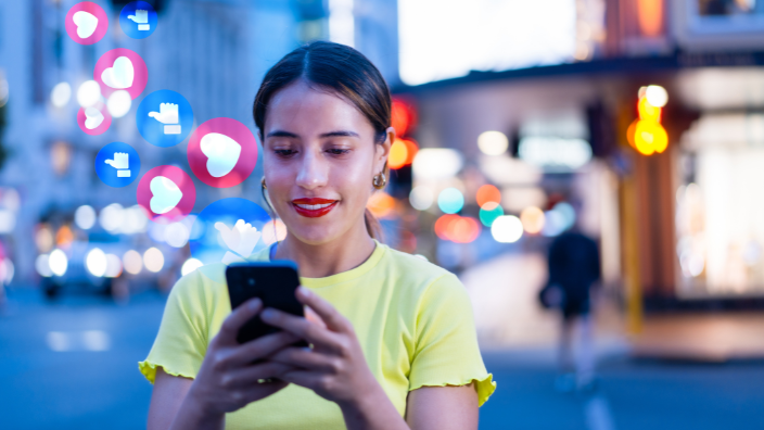 An image of a woman looking at her phone, social media icons emerge from her phone.