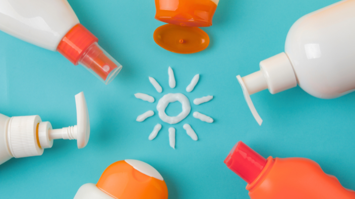 An image of six different sunscreen bottles placed in a circle with their nozzles facing each other. Lotion sunscreen is used to draw a sun in the middle of the bottles.